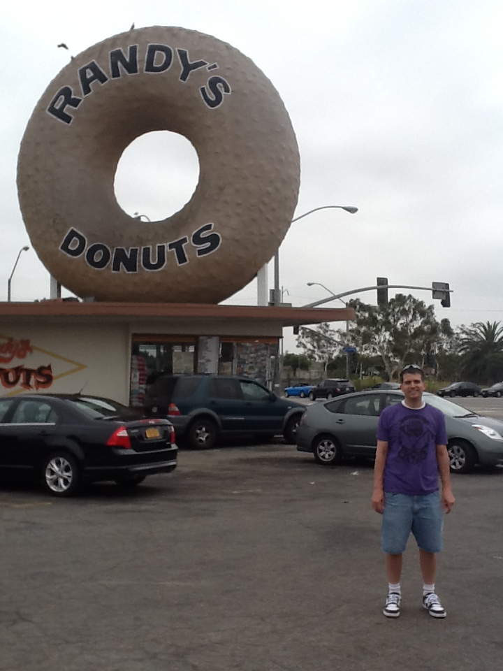 a man standing in front of a large donut sign