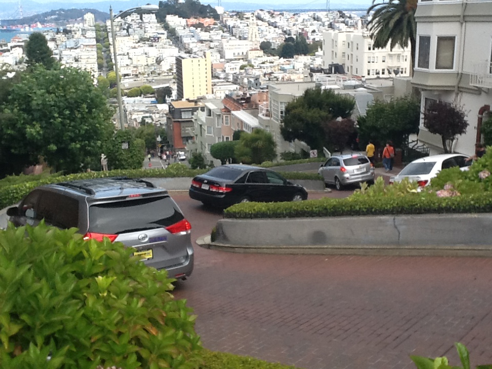 cars parked cars on a road with Lombard Street in the background